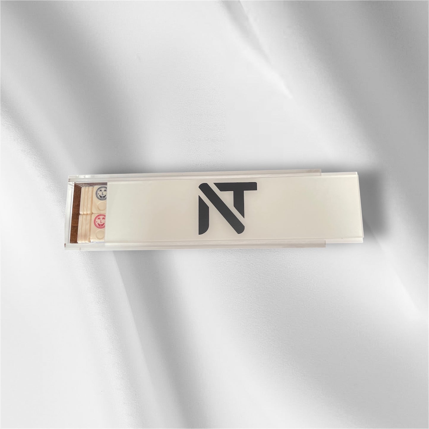 A slim rectangular product box with a clear lid and a black stylized 'NT' logo on the front, photographed on a soft white fabric background with gentle shadows.