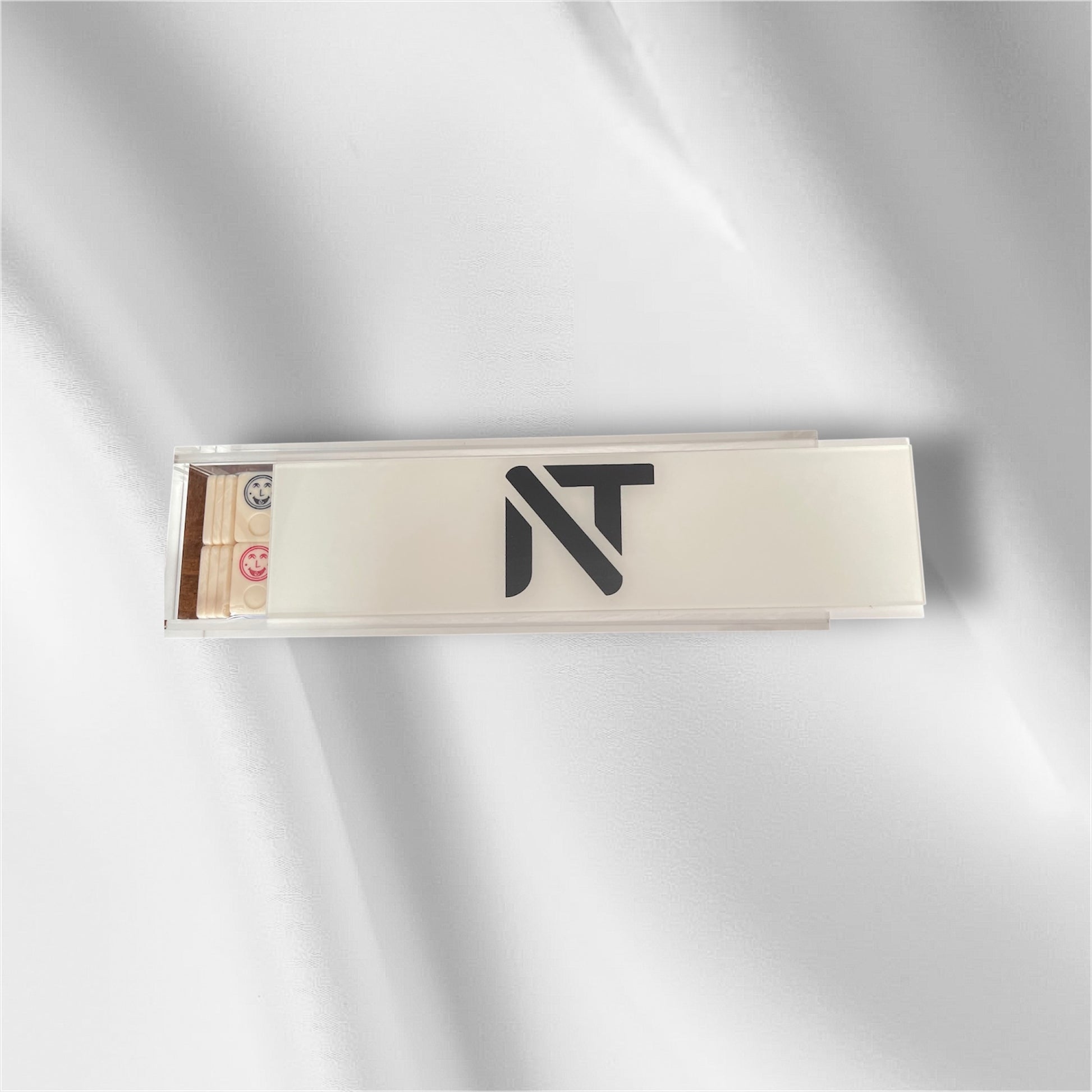 A slim rectangular product box with a clear lid and a black stylized 'NT' logo on the front, photographed on a soft white fabric background with gentle shadows.