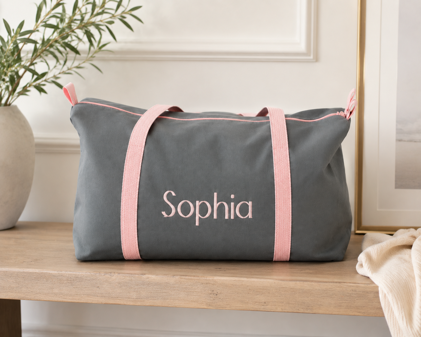 Gray duffel bag with pink straps and 'Sophia' branding on a wooden surface.